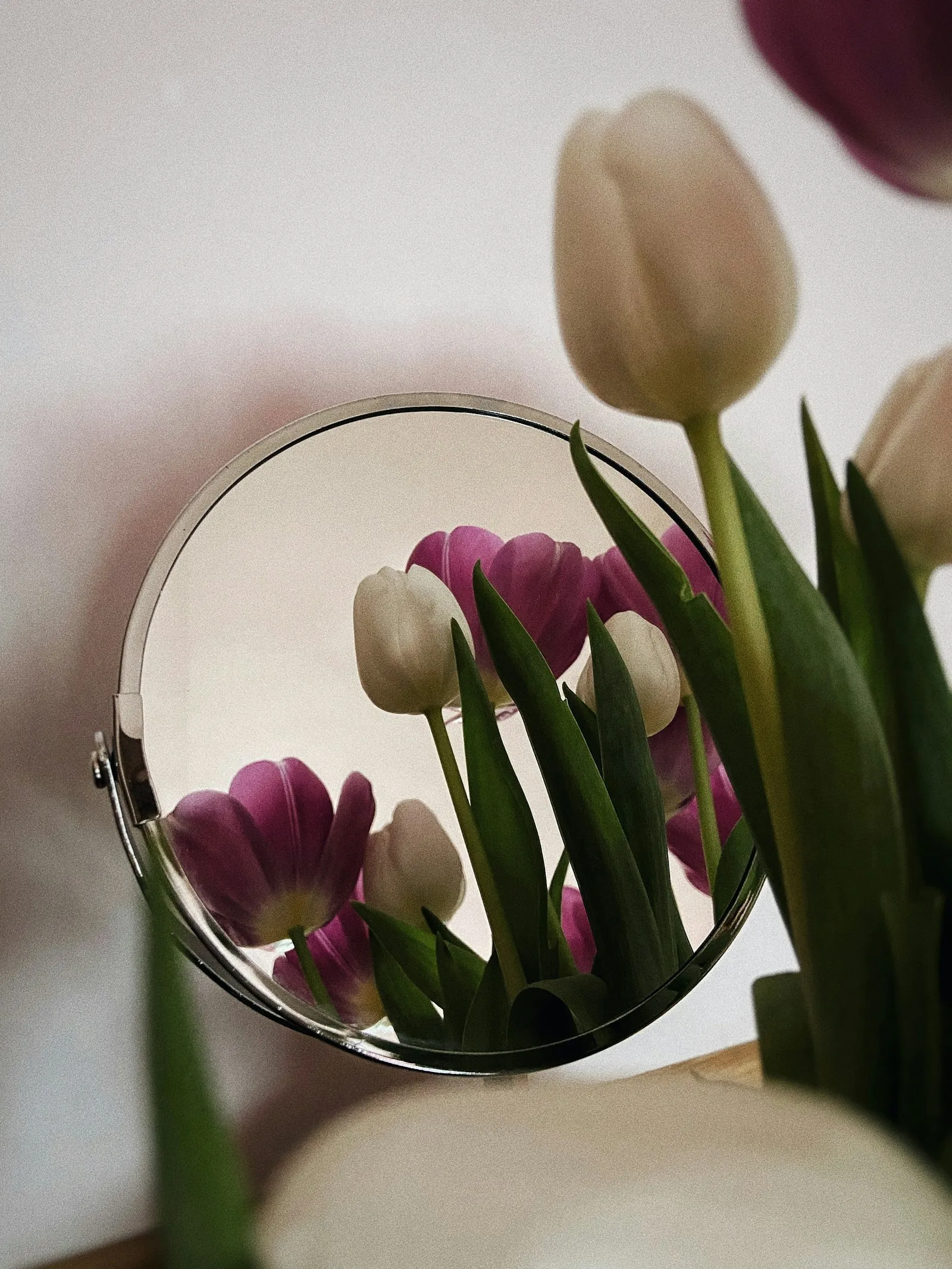 A round mirror beside fresh pink and white tulips